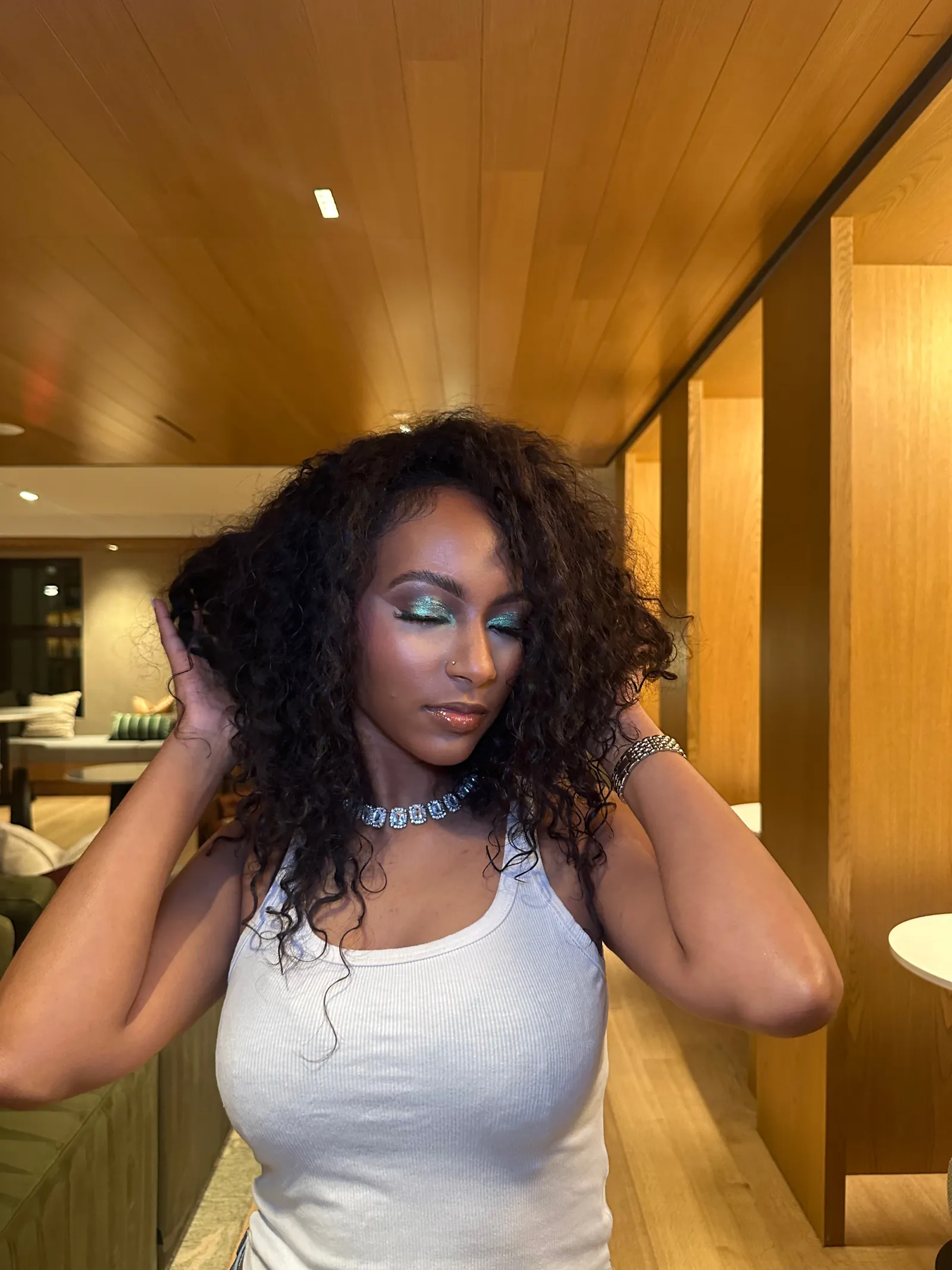 Teal shimmer eyeshadow, glowing skin and glossy lips, eyes closed, hands in her curls