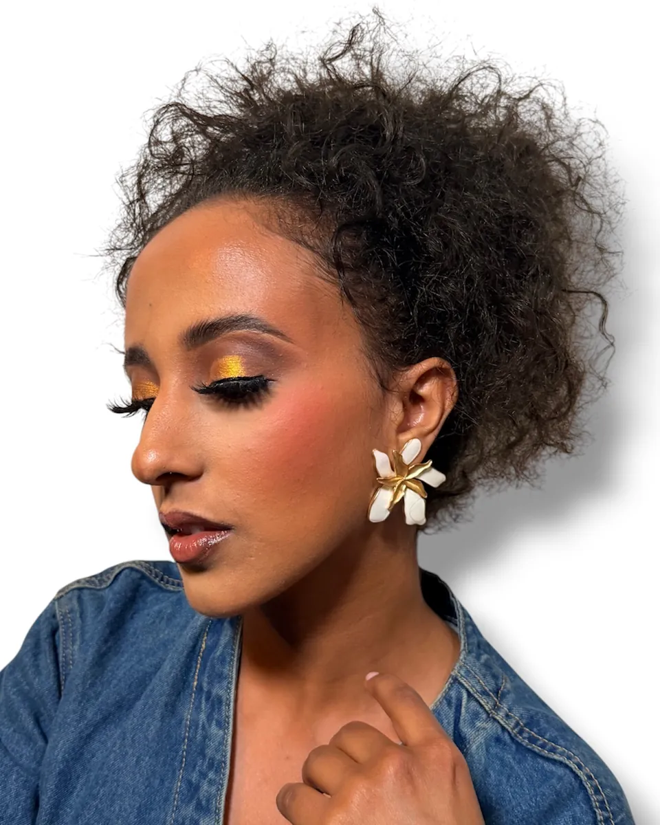 Profile of a woman with golden eyeshadow, winged liner and a flower earring