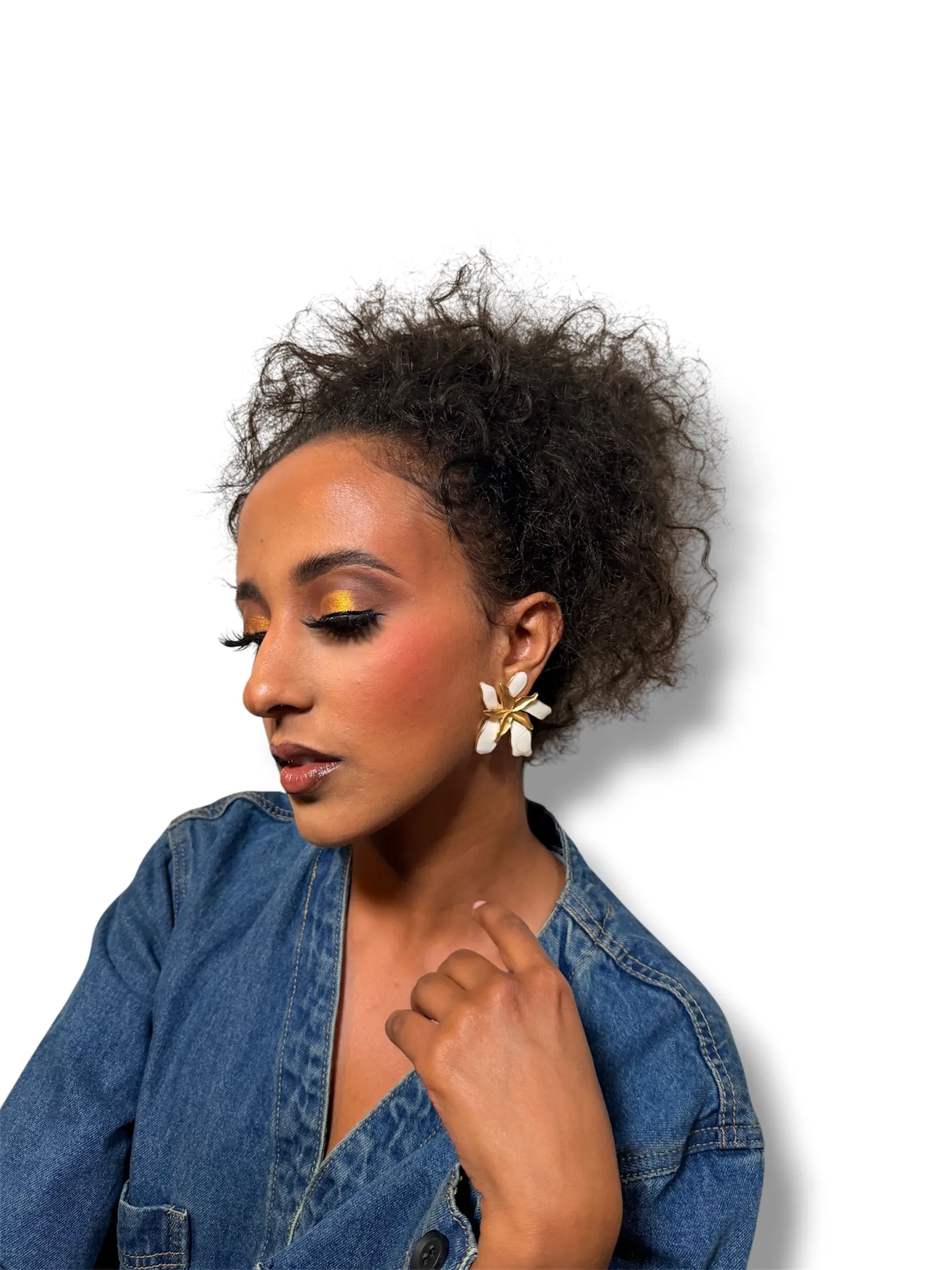 Profile with golden eyeshadow, winged liner and lashes, a flower earring and a denim jacket