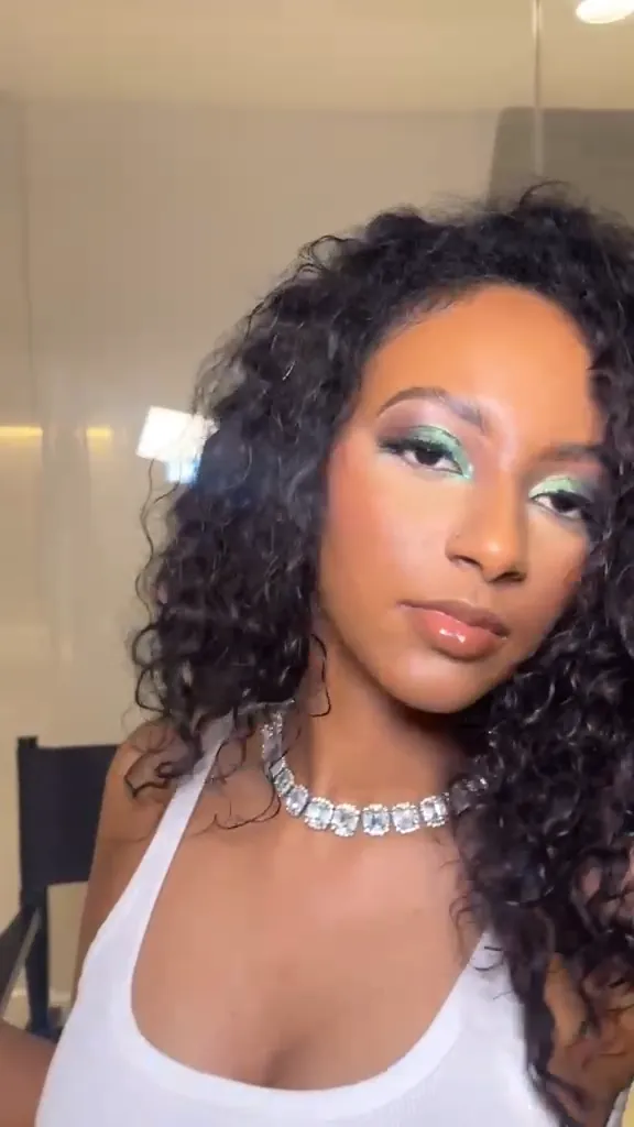Close-up of teal eyeshadow, glowing skin and glossy lips, the head turning