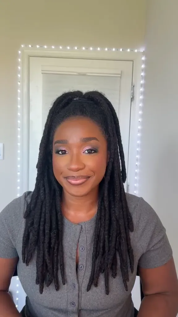 Smiling woman with locs and a soft, glowing makeup, seated facing the camera