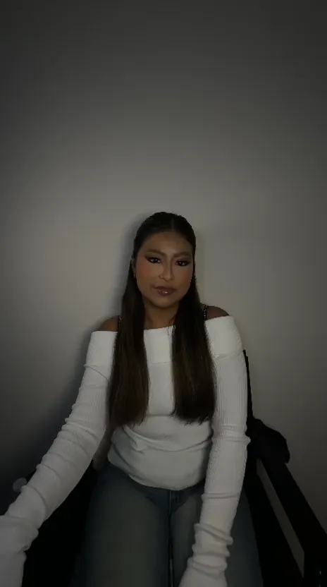 Woman in a white off-shoulder sweater posing in a chair against a grey backdrop