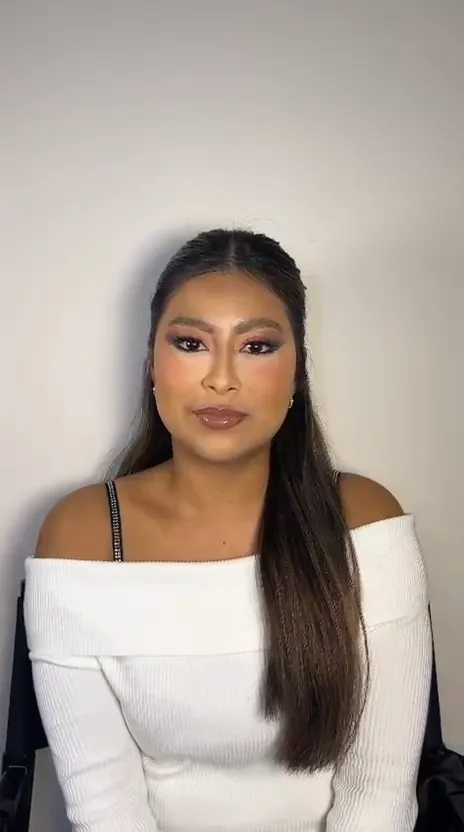 Close-up of a woman in a white off-shoulder top: pink eyeshadow, winged liner, lashes and glossy lips