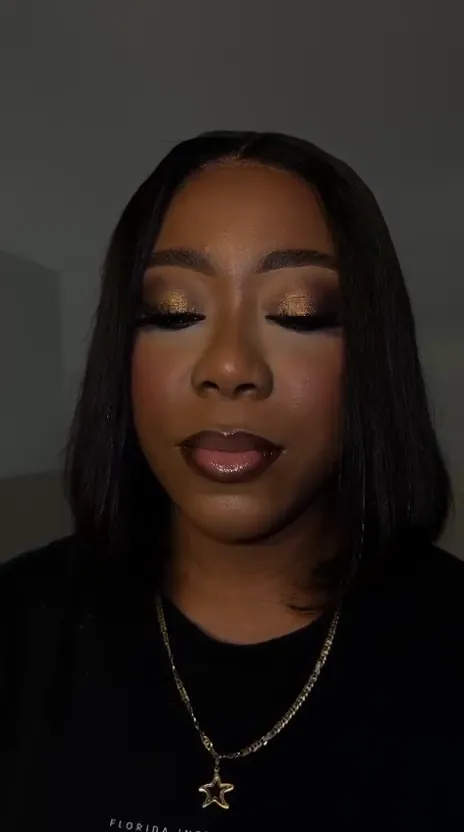 Woman with a black bob, golden smoky eyeshadow and long lashes, closing and opening her eyes